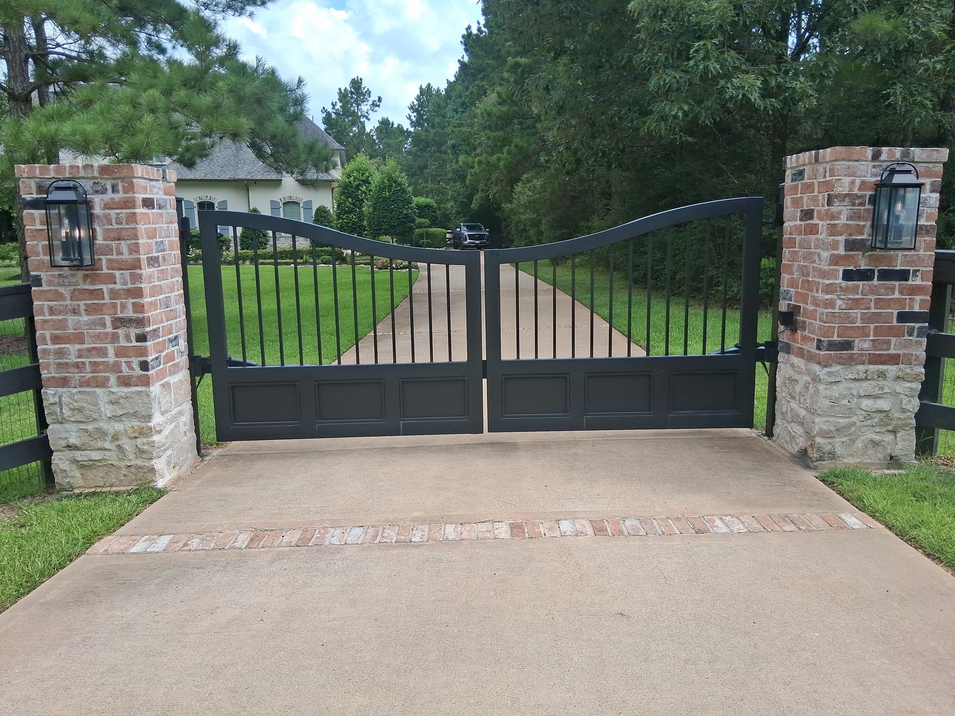 Custom arched steel driveway gate between brick pillars, fabricated and installed by Affordable Texas Steel in Magnolia, TX